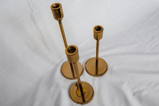 Set of three gold candle holders on a white fabric background